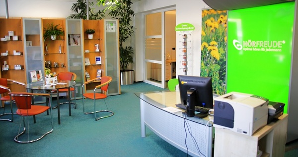 Modernes Hörakustik-Fachgeschäft mit Beratungstresen, Infomaterial und grüner Werbewand.